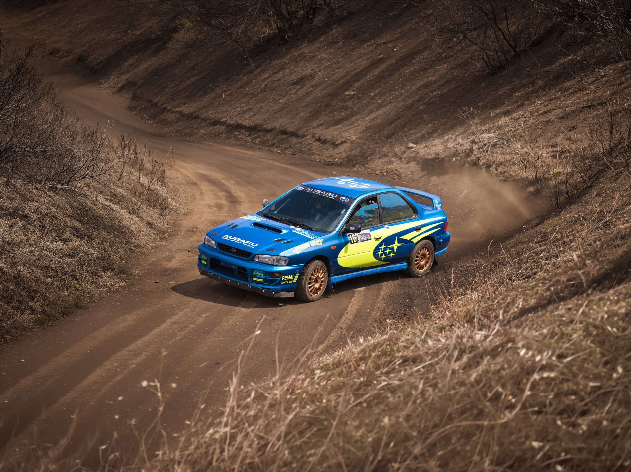 Classic Subaru Impreza WRX STI rally car driving on a dirt road during a stage event