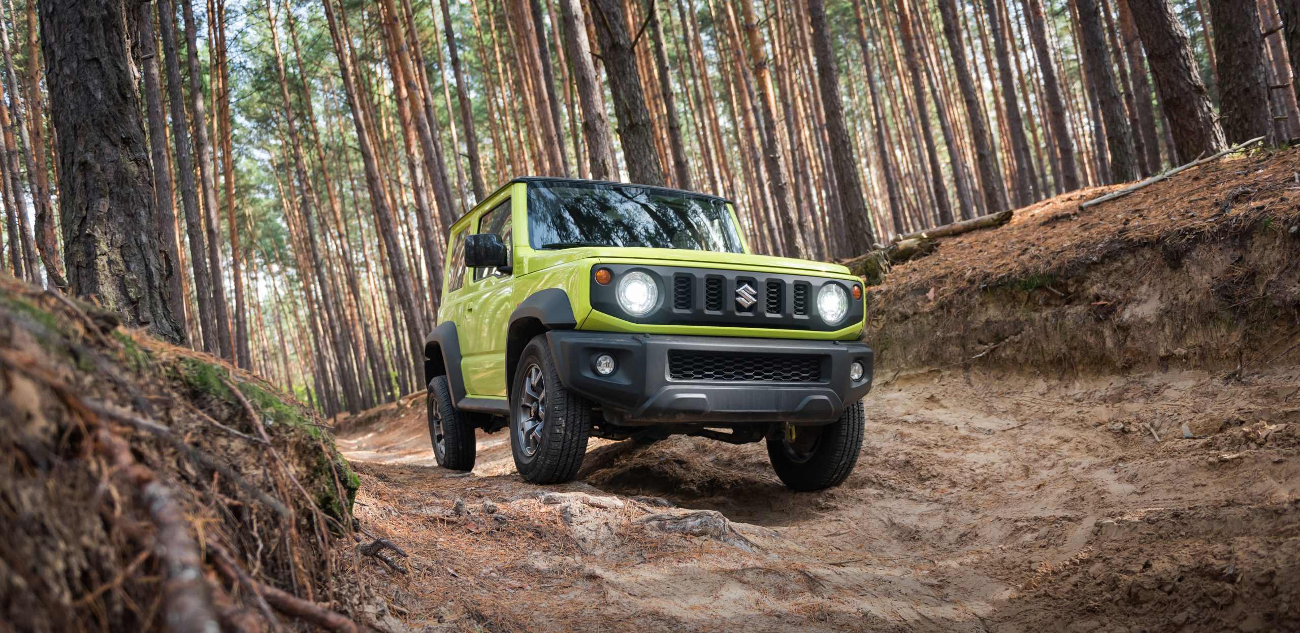 Green Suzuki Jimny driving off road through forest terrain showcasing compact 4x4 capability